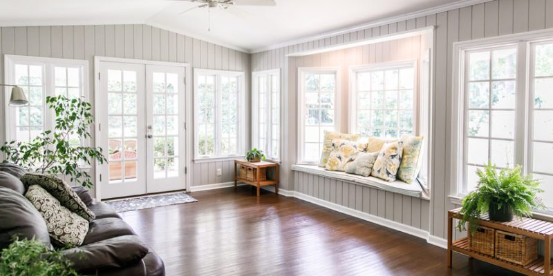 A remodeled living room with wooden flooring, large windows, and neutral-toned wall paneling, showcasing a blend of comfort and modern design.
